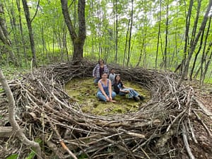 all four research team members sit smiling inside a giant nest in the forest